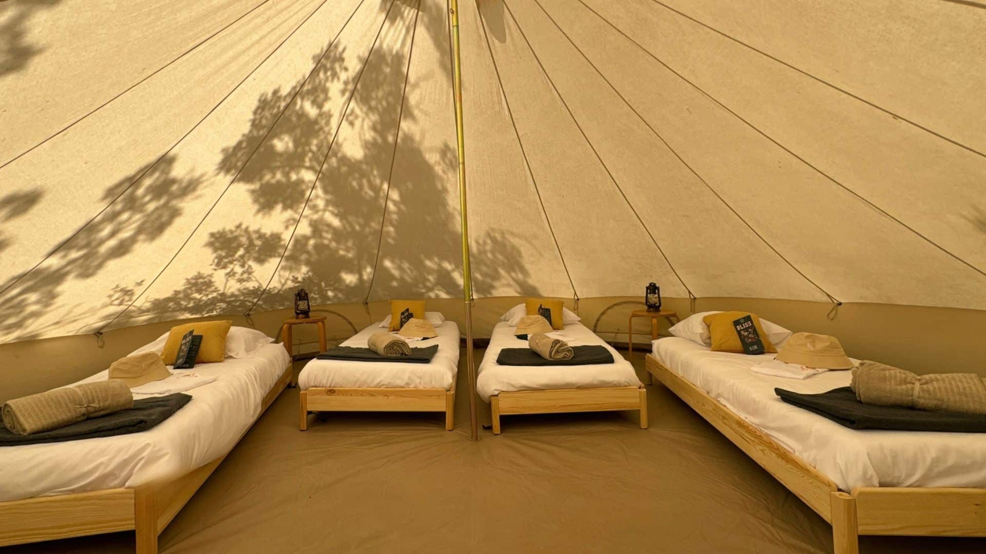 Intérieur d’une tente tipi lodge confort + aménagée avec 4 lits en bois modulables en lits doubles ou simples, offrant un hébergement spacieux et flexible pour les invités