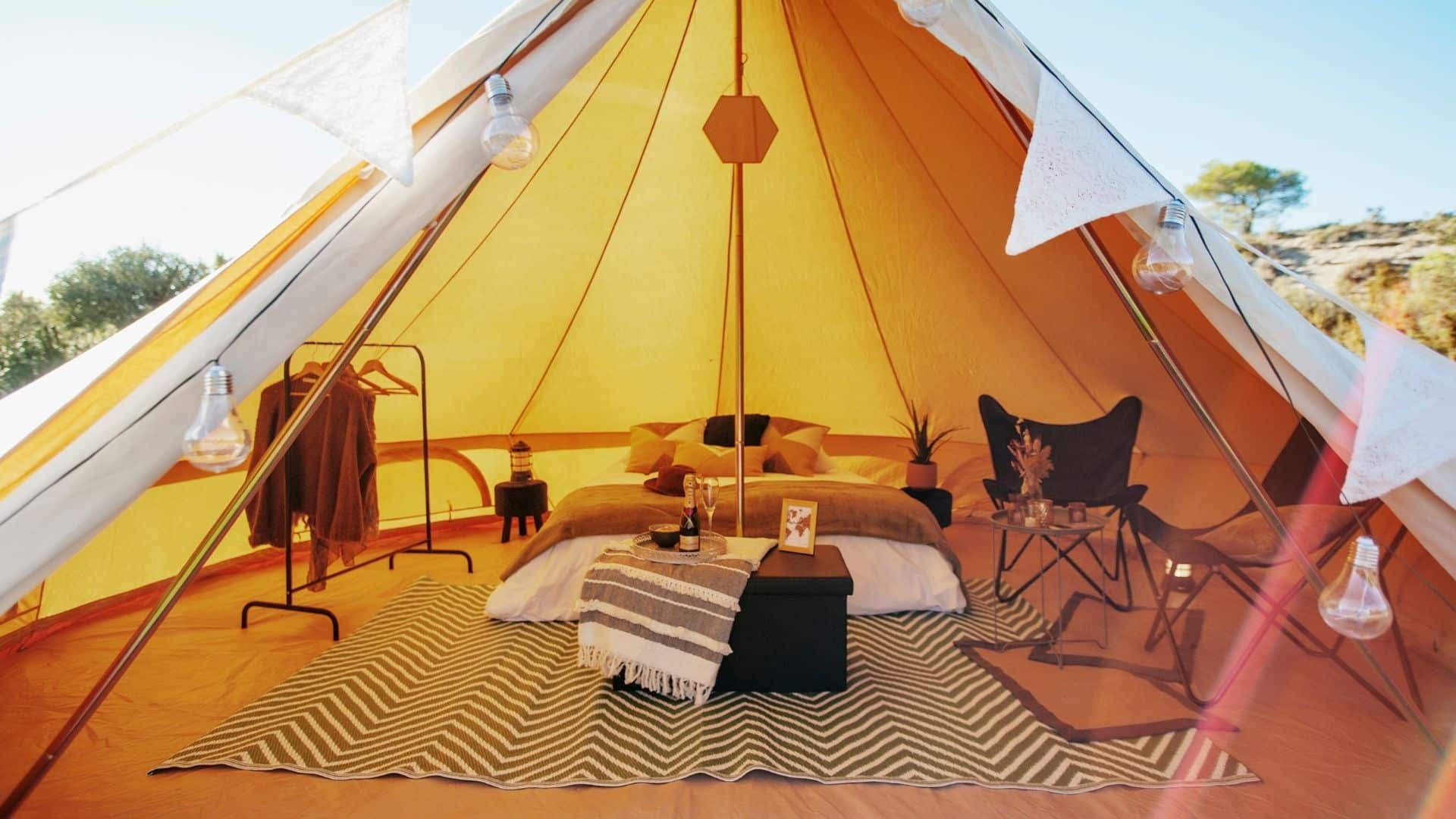 Intérieur d’un tipi lodge de luxe avec ameublement complet, comprenant un lit en bois, un petit salon, et un porte-vêtements, idéal pour héberger des invités lors d’événements privés, séminaires ou anniversaires haut de gamme.